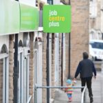 an adult holding a child's hand as they walk down a pavement outside a job centre plus