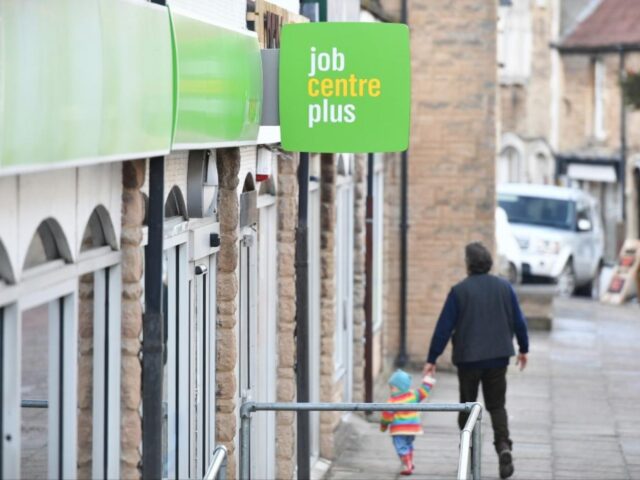 an adult holding a child's hand as they walk down a pavement outside a job centre plus