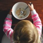 girl eating cereal in white ceramic bowl on table