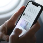 A phone being held in two hands as someone scrolls, the phone open on Twitter