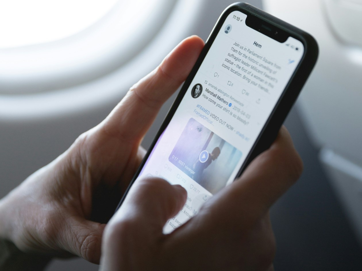 A phone being held in two hands as someone scrolls, the phone open on Twitter
