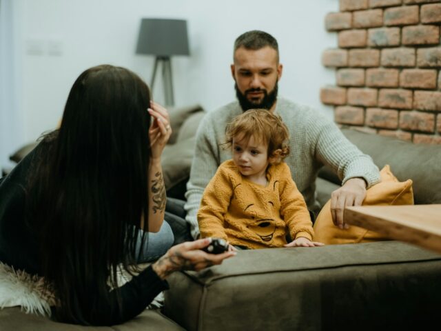 a man and woman sit either side of a young girl on a sofa
