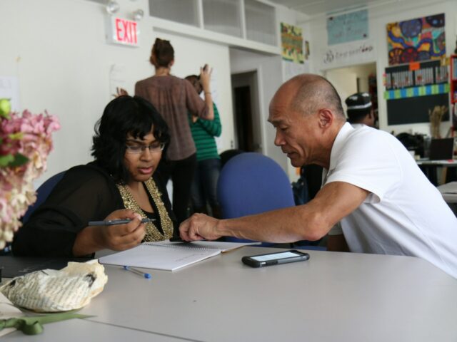 Two people at a table, one instructing the other in book-keeping